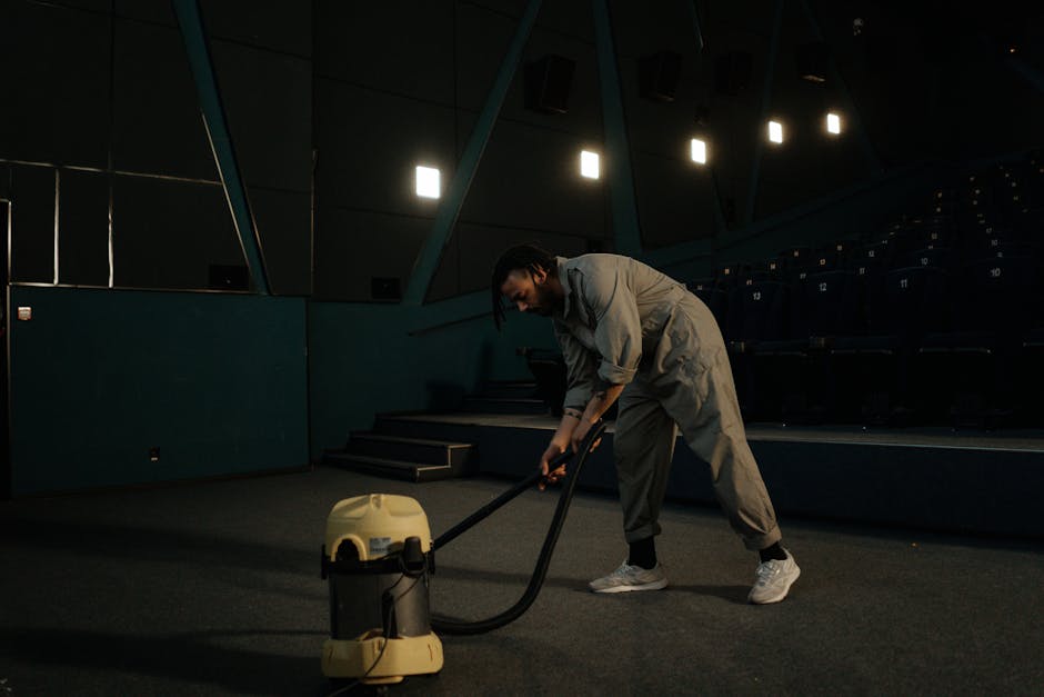 A person is engaged in domestic surface cleaning by using a vacuum cleaner on a decorative aspect of a patterned area rug with floral motifs in shades of beige, green, and orange. The individual, dres